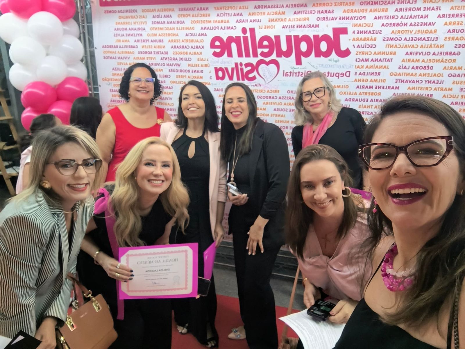 Mulheres celebrando uma homenagem diante de um painel rosa
