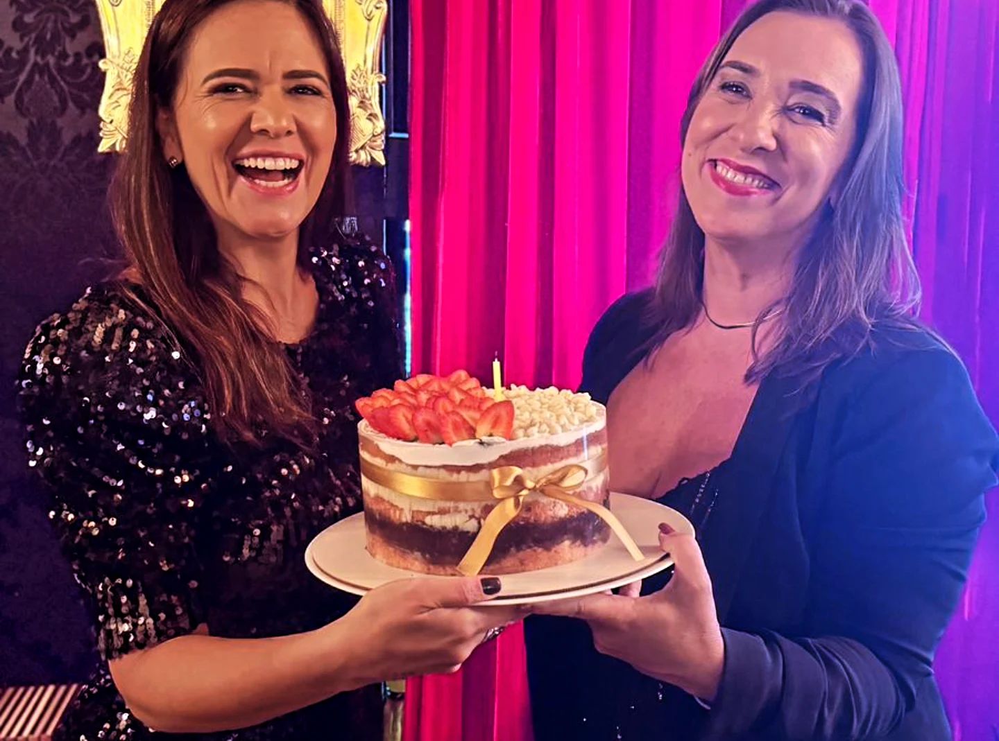 Duas mulheres sorrindo enquanto seguram um bolo de aniversário
