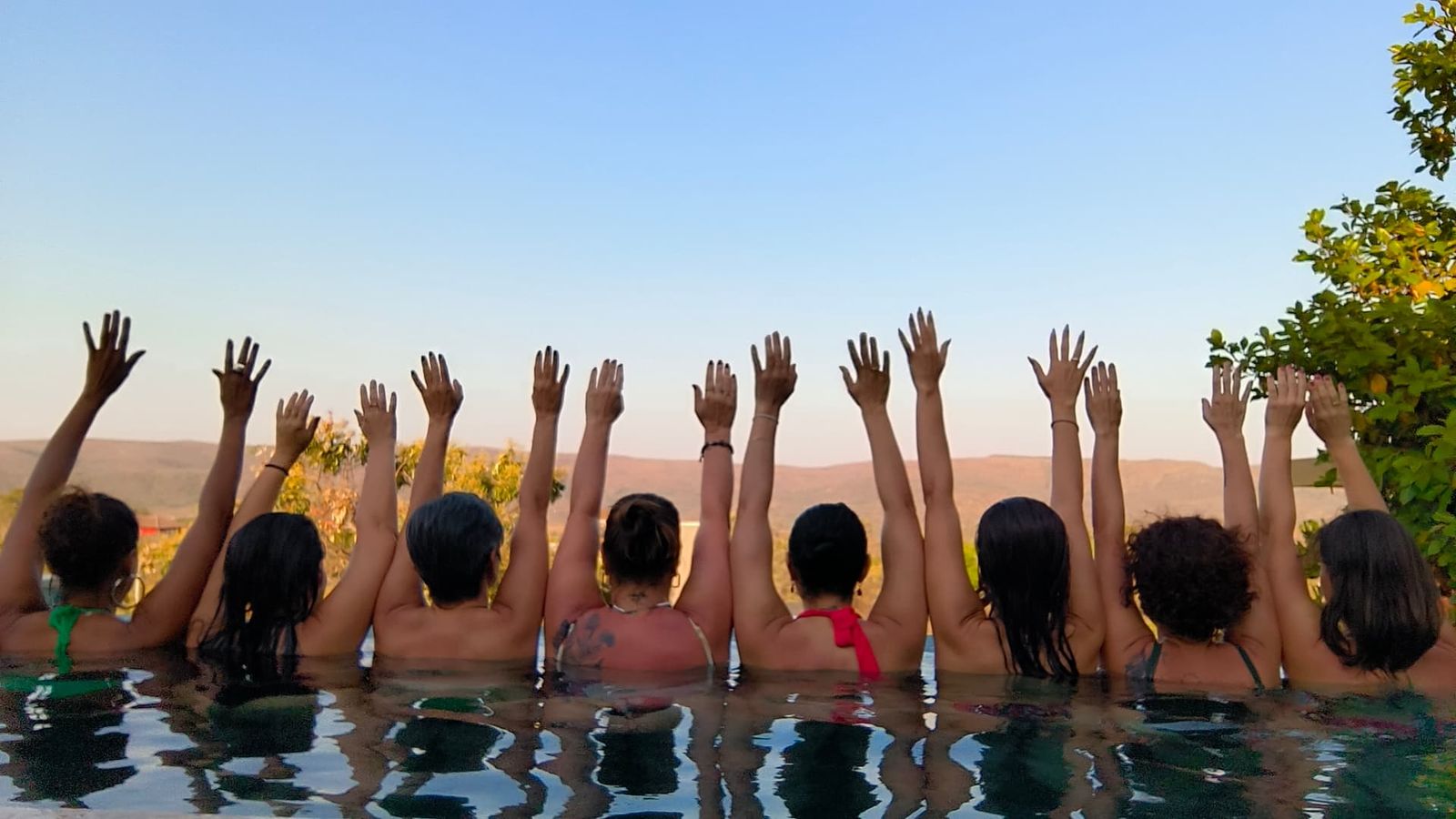 Mulheres de costas com os braços erguidos em uma piscina com vista para as montanhas